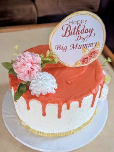 A round birthday cake displays a textured white exterior with a vibrant orange drip icing cascading down the sides