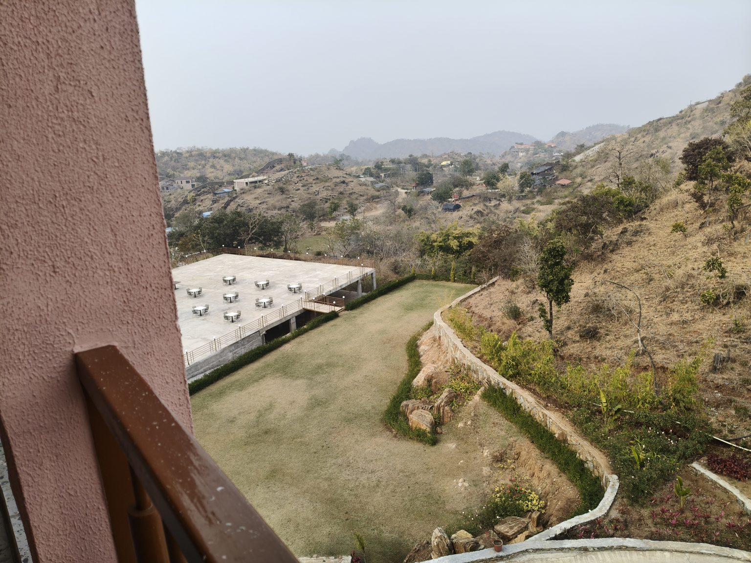 Balcony overlooking a green lawn, winding path, hills, and distant buildings.
