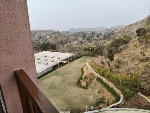Balcony overlooking a green lawn, winding path, hills, and distant buildings.
