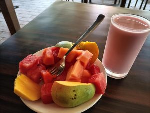 A white plate holds a colorful assortment of fresh fruit, including large chunks of red watermelon, orange papaya, and slices of yellow mango.
