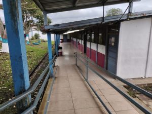 Covered school walkway with classrooms and a grassy courtyard.
