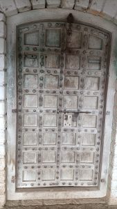 Old arched wooden door with faded blue and white paint, metal studs, and a rusted lock in a stone wall.