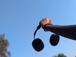 A hand holding headphones with a sky blue background 
