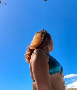 Person with red hair viewed from behind, looking at a blue sky.