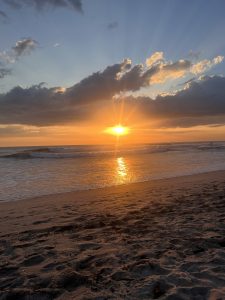 Sunset over the beach with golden light reflecting on the ocean and colorful clouds in the sky.