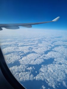 Airplane wing above a vast layer of fluffy white clouds under a deep blue sky.