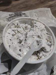 Chocolate-speckled ice cream in a paper cup with a small spoon.

