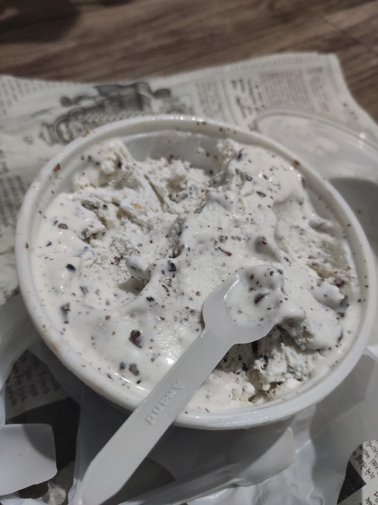 Chocolate-speckled ice cream in a paper cup with a small spoon.