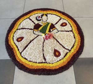A colorful circular rangoli featuring a traditional figure surrounded by vibrant floral patterns.