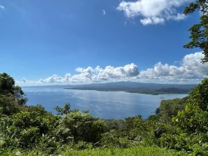 
A calm bay surrounded by tropical greenery and mountains under a blue sky with white clouds.