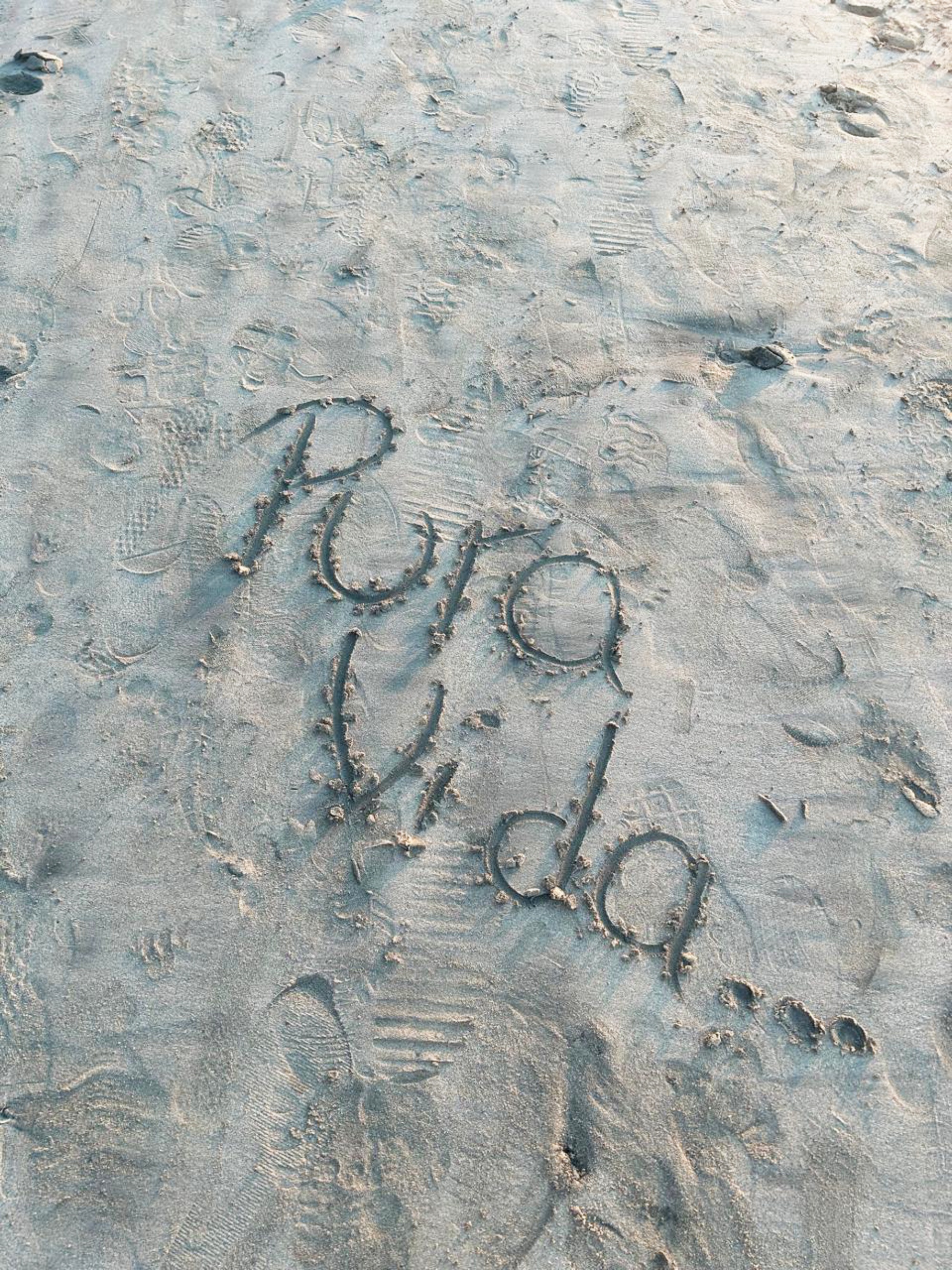 The words "Pura Vida" written in the sand on a beach.