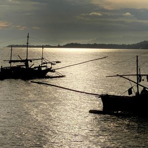 Two fishing boats head across the calm sea, carried by the gentle afternoon waters.