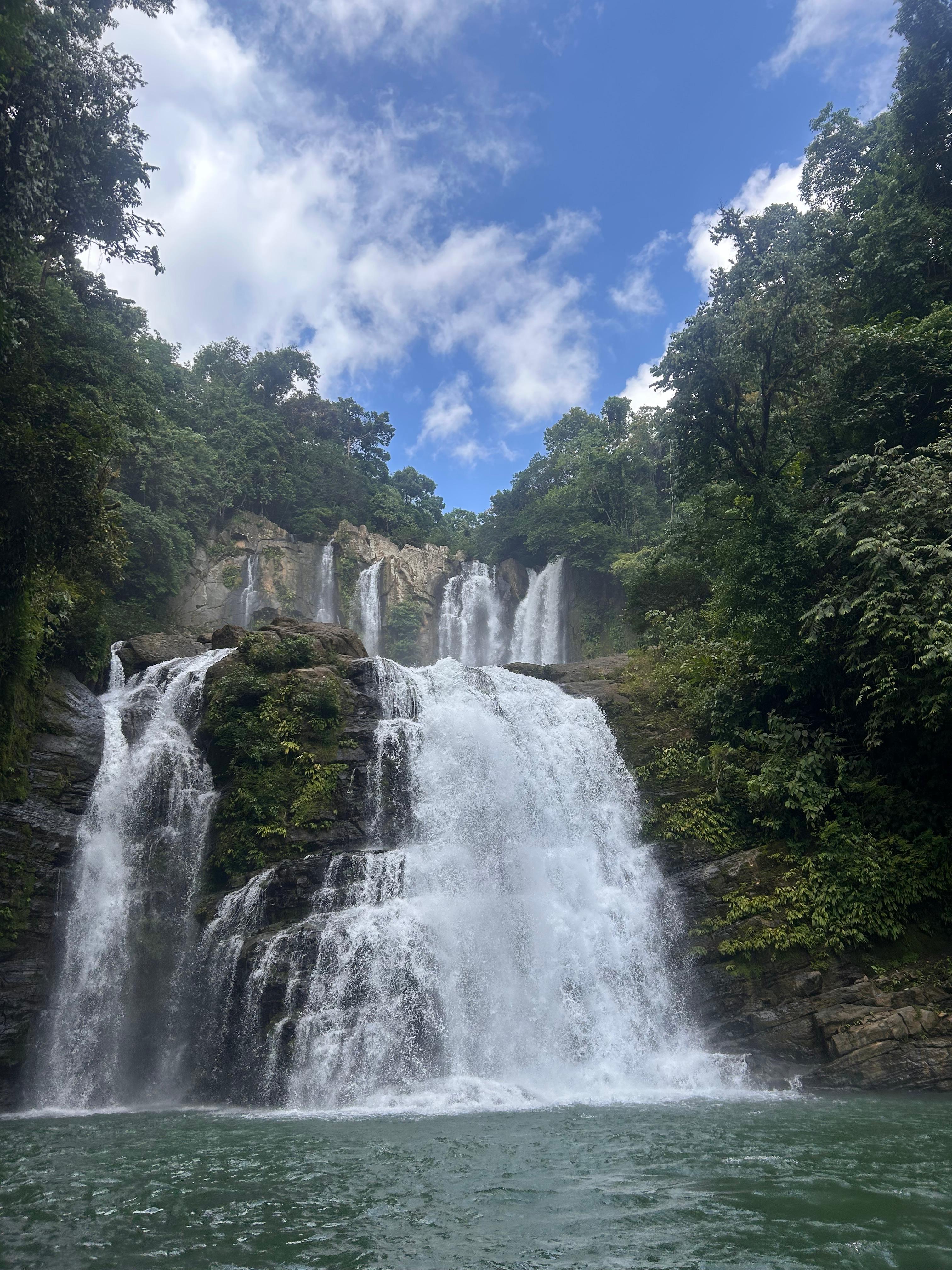A waterfall flowing into a turquoise pool, surrounded by green trees.