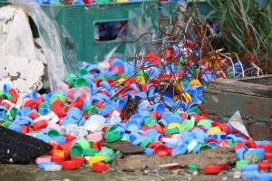 A pile of colorful plastic bottle caps, rusted wire, and garbage dumped on the ground.