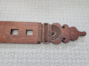 A large turquoise wooden chest with a woven-style carved front stands against a patterned wall. Its bright color, aged finish, and detailed wooden design contrast beautifully with the blue-and-white patterned floor. It was part of the traditional weaving machine (wooden loom). Captured in Palazhi, Kozhikode, Kerala. 