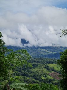 Low clouds drift across lush green mountains, partially veiling the landscape and creating a peaceful scene in the tropical highlands.
