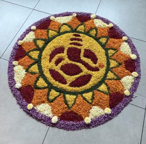 A colorful floral arrangement featuring Lord Ganesha, surrounded by red, orange, green, and white petals.