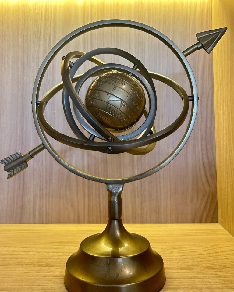 Decorative bronze globe with metallic rings and arrows on a polished base.