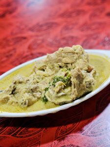 A plate of chicken kurma features tender chicken pieces in a thick, creamy yellow-green gravy, garnished with fresh herbs. The close composition highlights the rich texture and inviting appearance of the dish. Captured in Koolimadu, Kozhikode, Kerala.