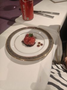 
A small dessert with red sauce is served on a decorative white plate.
