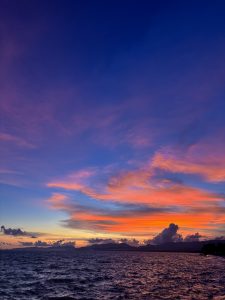 The mixture of purple and orange skies above the calm deep blue sea.