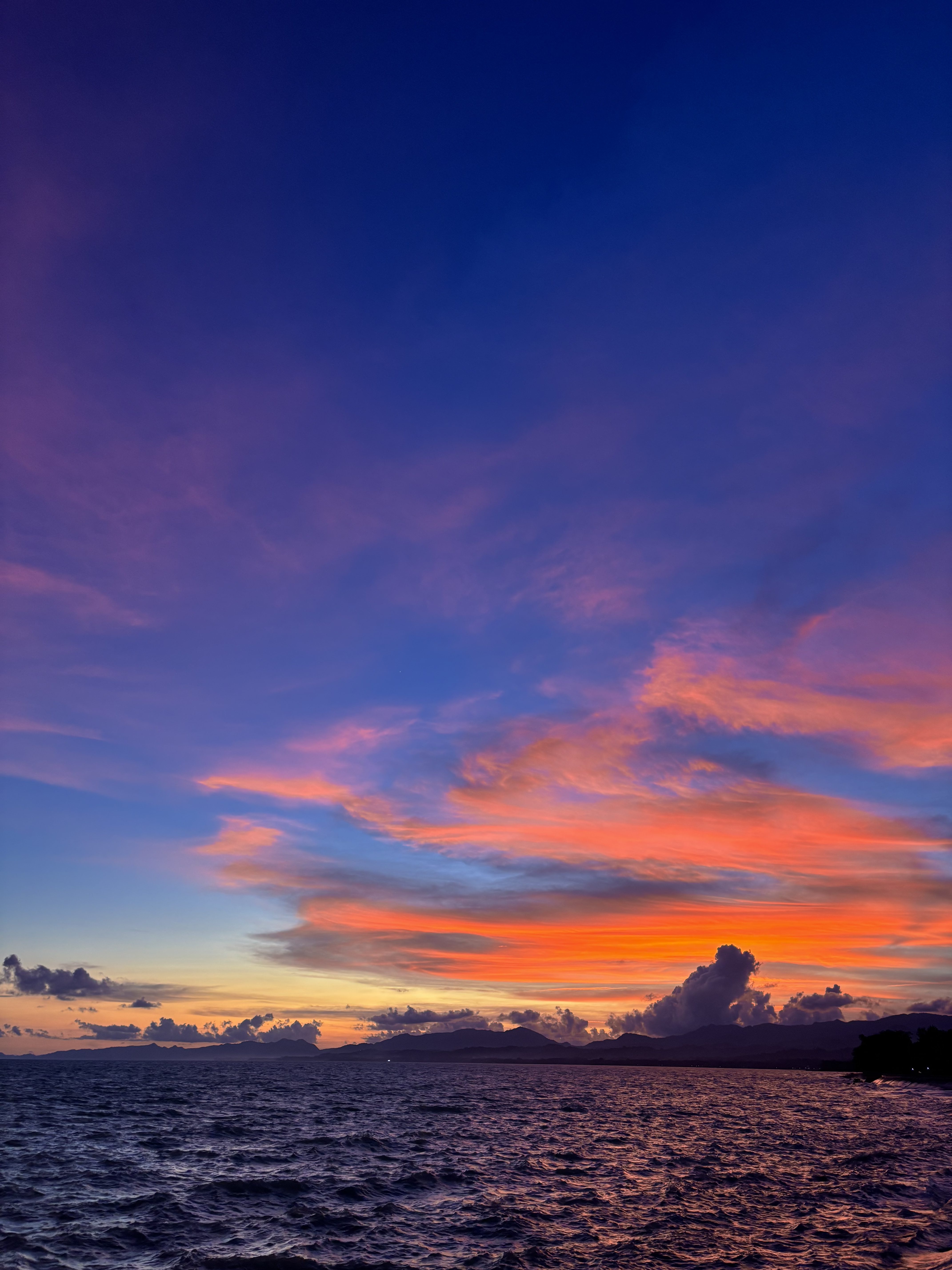 The mixture of purple and orange skies above the calm deep blue sea.
