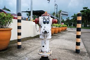A fire hydrant painted as a Dalmatian with black spots and face details on a concrete walkway.