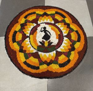A colorful circular rangoli featuring a dancer surrounded by bright geometric and floral patterns.
