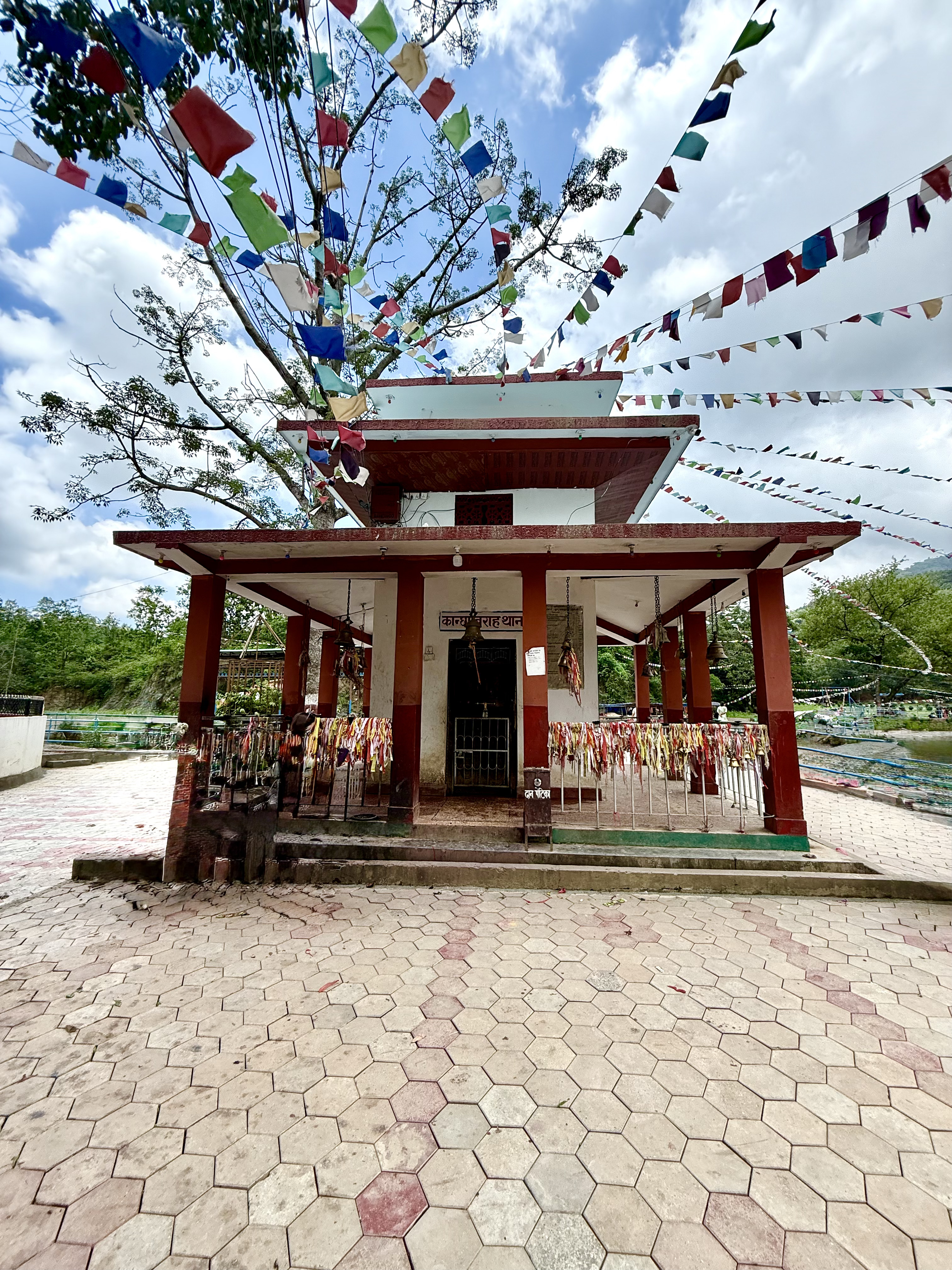 Barakune Temple with red columns, prayer flags, and a tiled pathway surrounded by greenery.