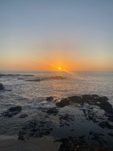 
Sunset over the ocean with rocky shore and gentle waves.