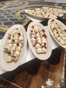 A platter of small square desserts topped with white meringue swirls and red raspberry garnish. Some pieces have small chocolate decorations.
