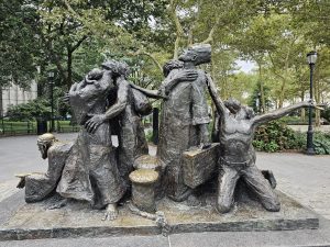 A bronze sculpture (The Immigrants) portrays immigrant families carrying their belongings, expressing hope, hardship, and determination. Surrounded by trees in a peaceful park, it reflects an important part of New York’s history. Captured in Battery Park, New York City, United States.
