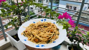 Stir-fried noodles with vegetables on a blue-patterned plate, held outdoors.
