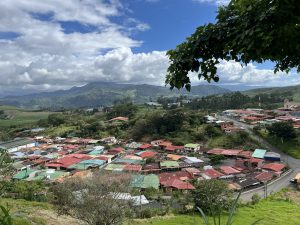 
A panoramic view of a small town nestled in a valley, surrounded by rolling green hills and mountains.