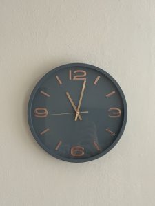 A round wall clock hangs against a textured light-colored wall.