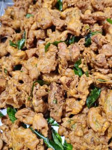 A close-up of assorted golden-brown fritters (Besan pakora) garnished with fresh curry leaves. The crispy textures, warm colors, and dense arrangement give the photograph a lively and appetizing look. Location: Pantheerankavu, Kozhikode, Kerala.