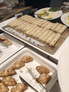 Layered finger sandwiches and almond croissants arranged on serving platters.
