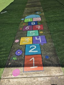 A colorful hopscotch game painted on a concrete path brings a playful touch to a green outdoor space, inviting children to enjoy simple moments of fun.
