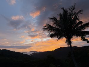 This stunning photograph captures a magical moment in Costa Rica. A fiery sunset paints the sky in vibrant shades of orange, red, and pink, while clouds swirl around the towering mountains.