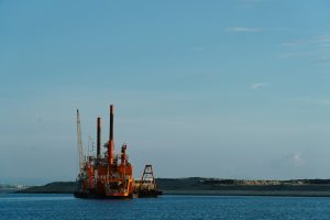 An orange dredger with three tall spud piles beside a sand reclamation bank in Manila Bay.