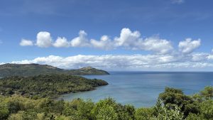 Scenic tropical coastline with lush green hills, turquoise bays, and a calm blue sea beneath puffy white clouds; peaceful, expansive view.