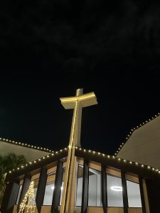 
Modern church lit at night with a glowing cross and Christmas lights.