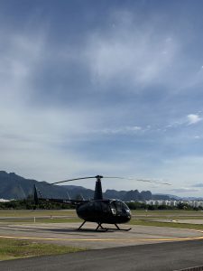 A sleek black helicopter is parked on a tarmac with a smooth gray surface, partially surrounded by a green grassy area.
