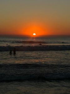 A peaceful beach sunset with ocean waves, a glowing orange sky, and two people standing in the water.