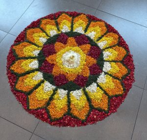 A colorful circular floral arrangement made of orange, red, yellow, and white petals in a symmetrical pattern.