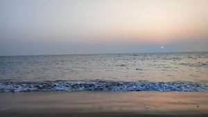 Saint Martin’s sea beach at sunset, with gentle waves rolling onto the sandy shore, a calm blue sea, and the sun setting near the horizon.