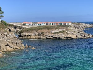 Row of traditional colorful fishing huts built on a rocky coastline overlooking bright turquoise ocean waters.