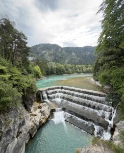 Clear river water flowing through lush green nature surrounded by forested mountains.
