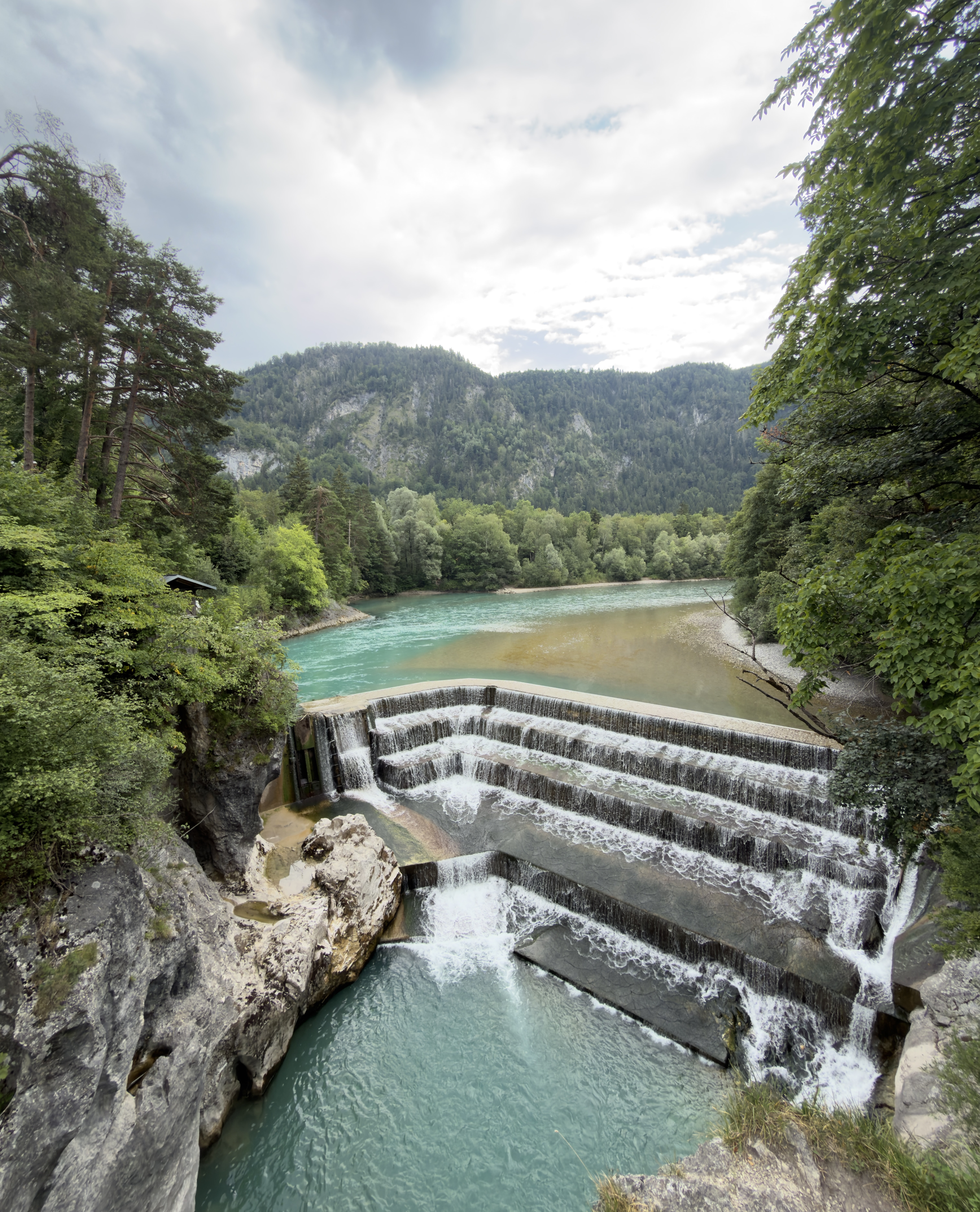 Clear river water flowing through lush green nature surrounded by forested mountains.