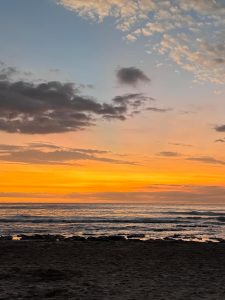 Sunset beach with calm waves, soft clouds, and warm orange, pink, and purple skies.